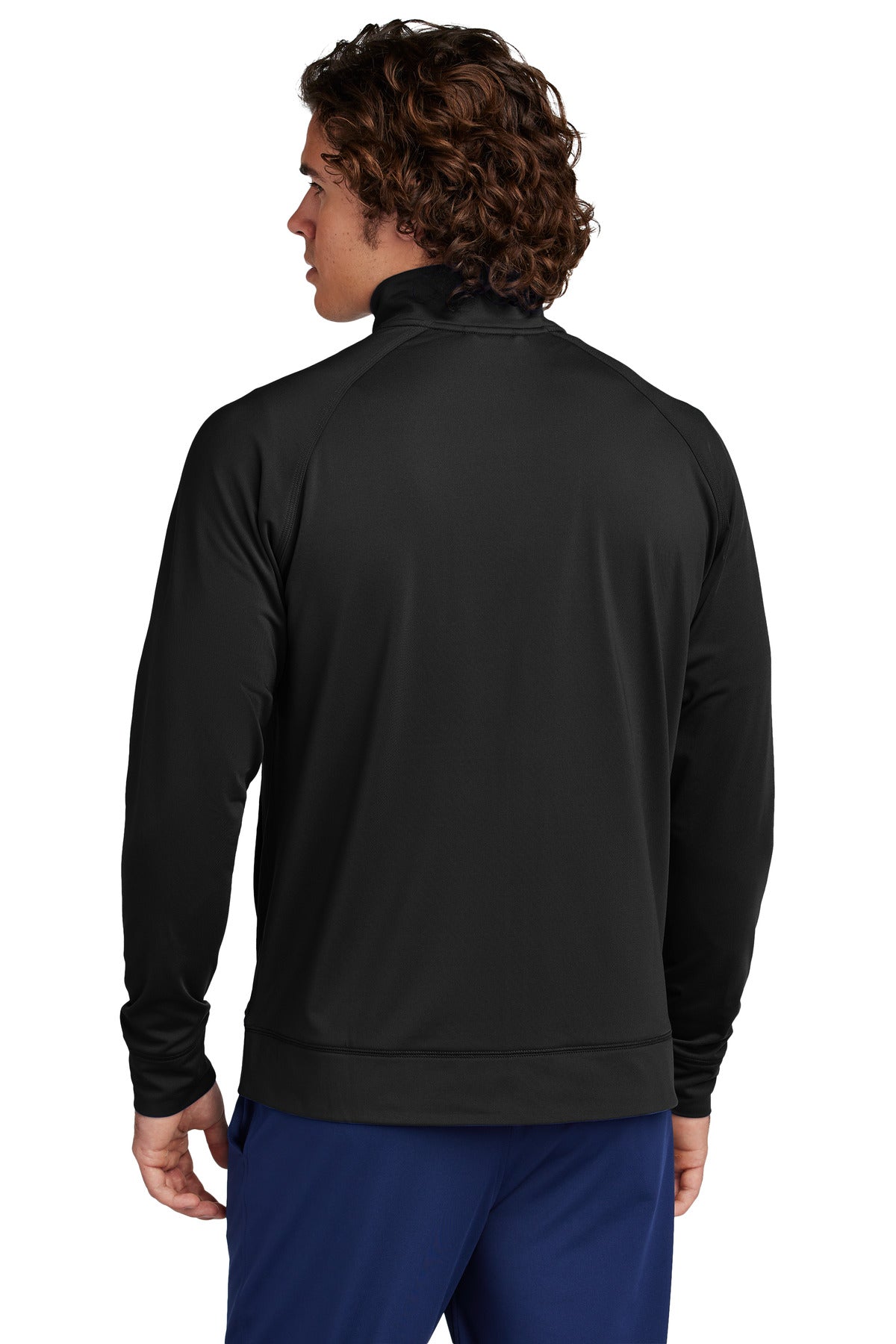 A man with curly brown hair, facing away from the camera, wears a black Creative Kids Learning Center Sport-Tek Sport-Wick Stretch Full-Zip Cadet Jacket ST857 and blue pants against a plain white background.