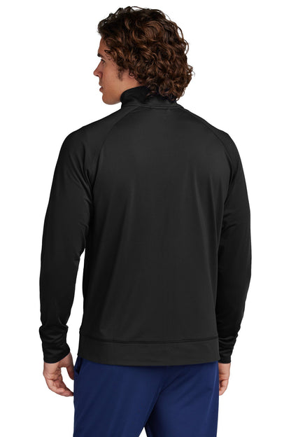 A man with curly brown hair, facing away from the camera, wears a black Creative Kids Learning Center Sport-Tek Sport-Wick Stretch Full-Zip Cadet Jacket ST857 and blue pants against a plain white background.