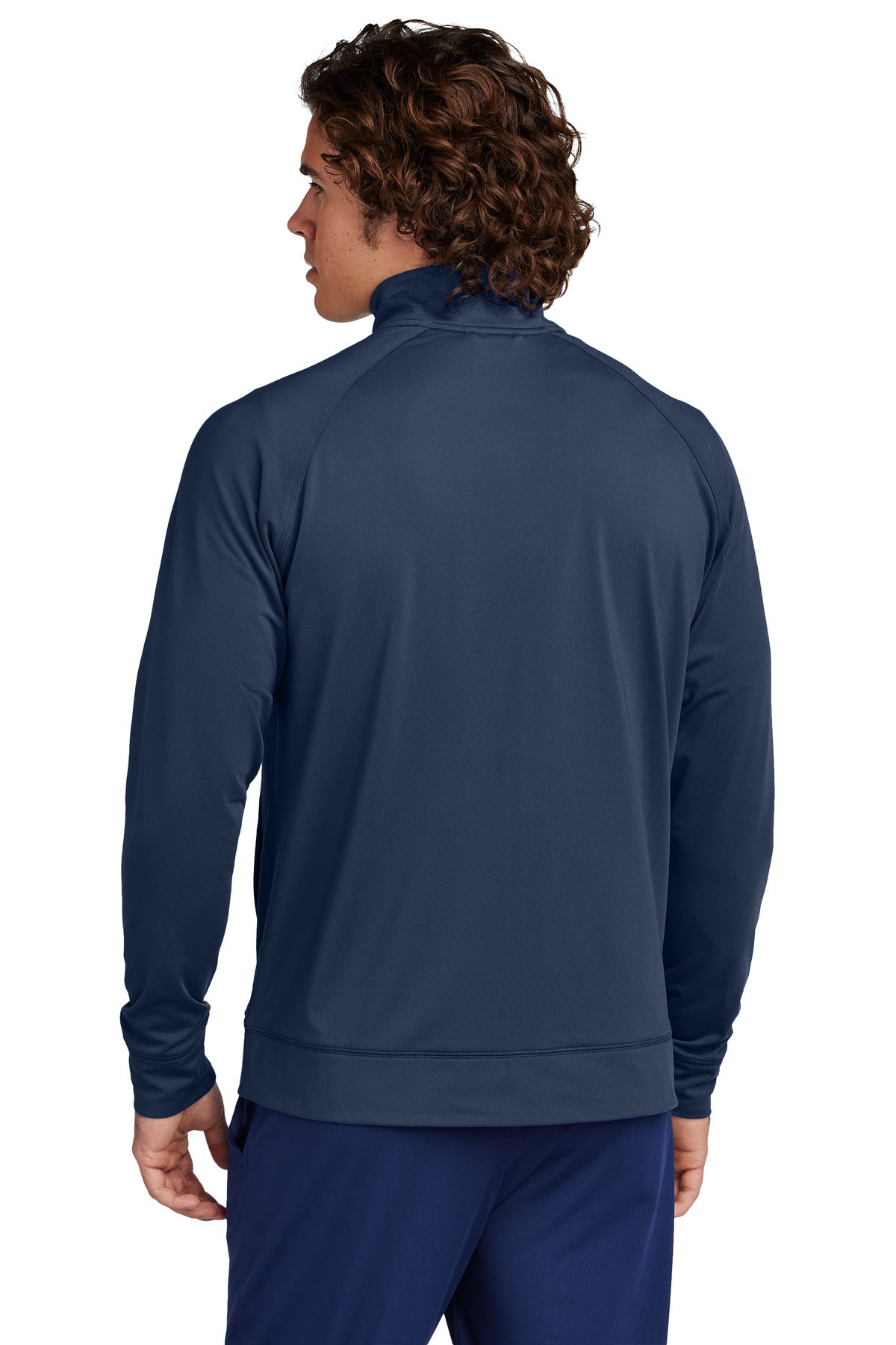 A man with curly brown hair, seen from behind, wears the CKLC Sport-Tek Sport-Wick Stretch Full-Zip Cadet Jacket ST857 in navy, featuring raglan long sleeves, a high collar, and matching pants.