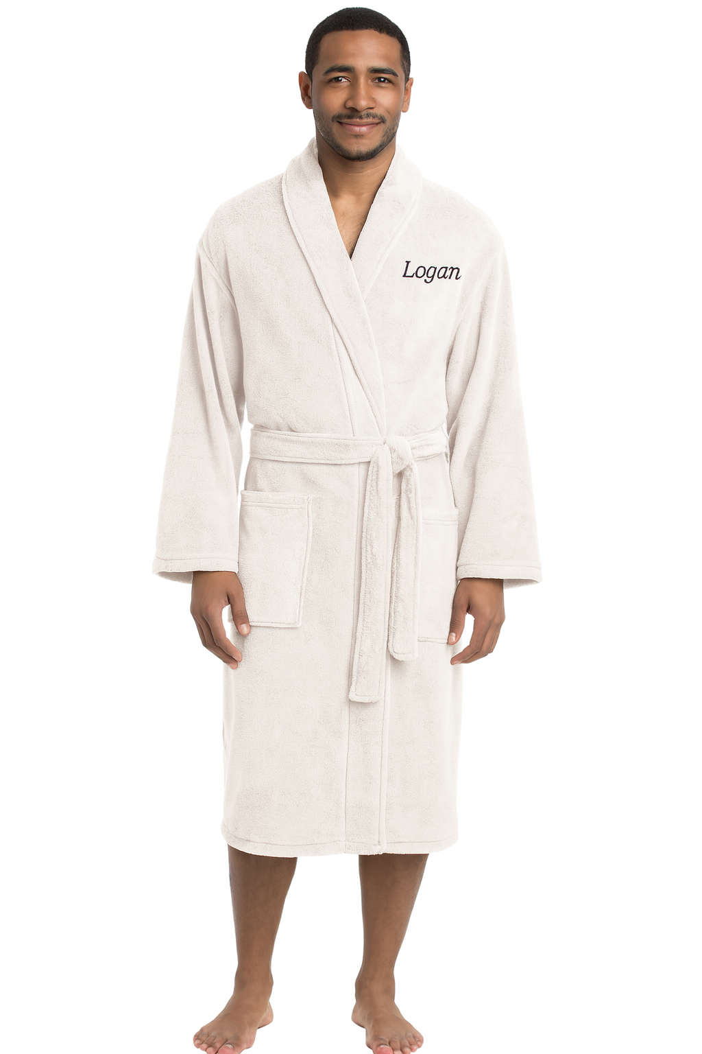 A man stands barefoot in a Personalized Plush Robe with "Logan" embroidered on the left chest. The light beige robe features a shawl collar, belt tie, and two front pockets, offering cozy luxury against a plain white background.