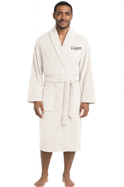 A man stands barefoot in a Personalized Plush Robe with "Logan" embroidered on the left chest. The light beige robe features a shawl collar, belt tie, and two front pockets, offering cozy luxury against a plain white background.