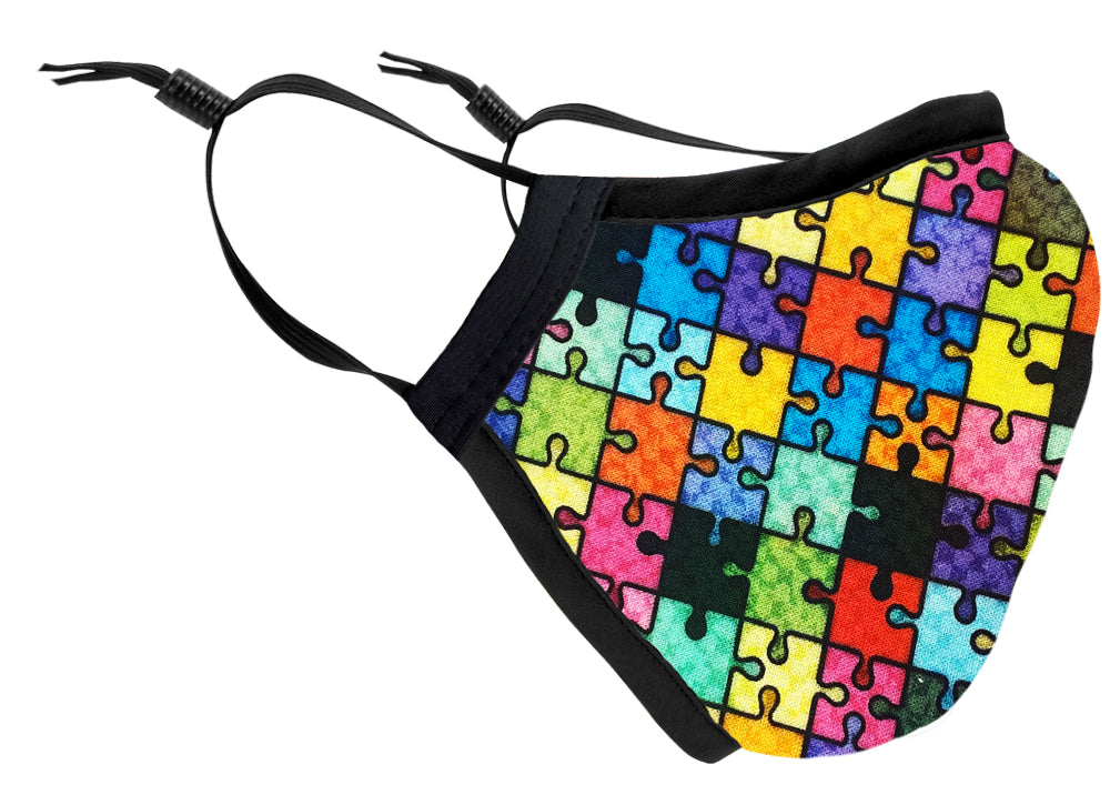 The Two Layer Fully Wired Protective Cloth Face Mask - Puzzle, Adult is made in the USA and features colorful interlocking puzzle pieces, black edges, adjustable straps, and a secure fit. Displayed on a white background.
